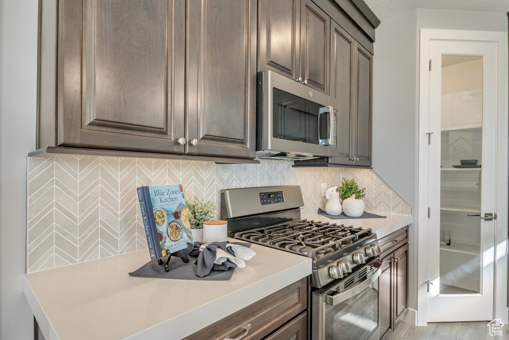 Kitchen featuring dark brown cabinetry, decorative backsplash, light hardwood / wood-style floors, and appliances with stainless steel finishes