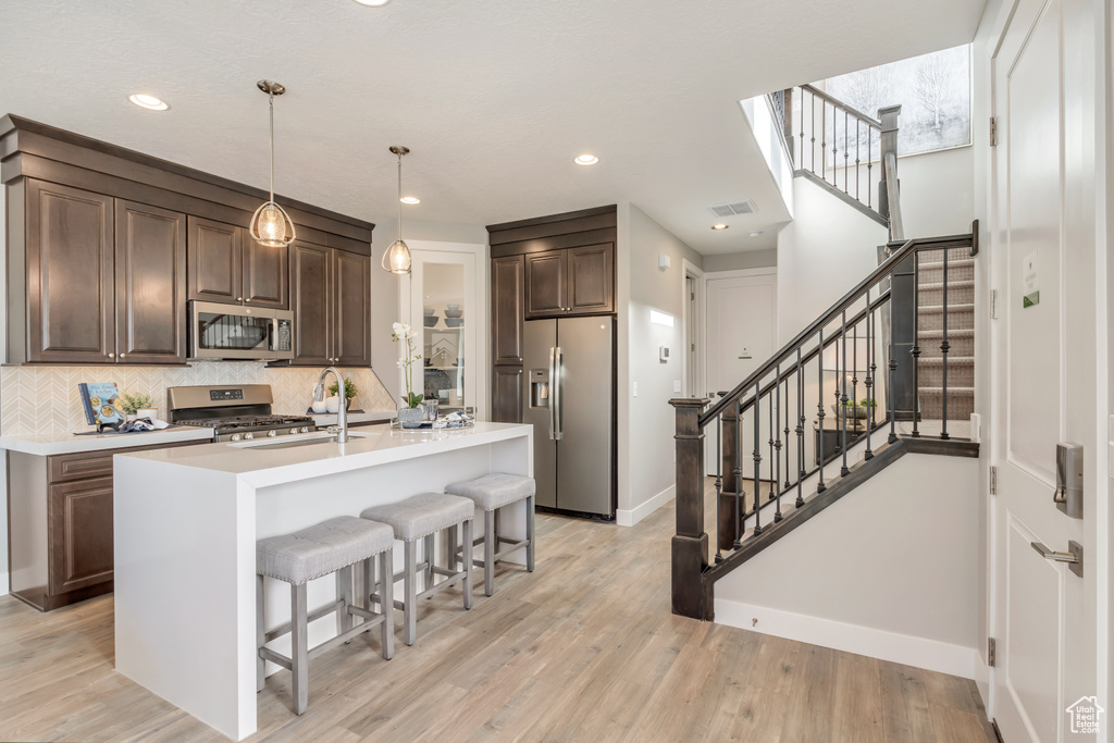 Kitchen with appliances with stainless steel finishes, decorative light fixtures, an island with sink, sink, and decorative backsplash