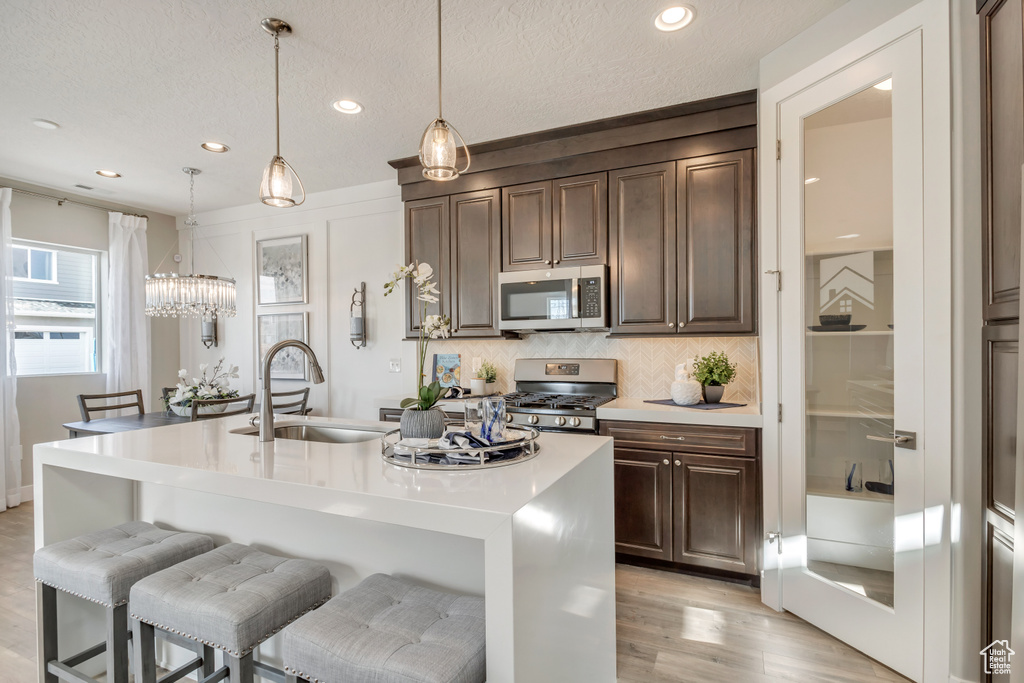 Kitchen with pendant lighting, sink, appliances with stainless steel finishes, an island with sink, and decorative backsplash