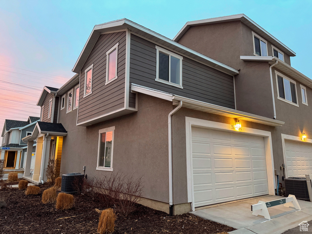 Property exterior at dusk featuring a garage and central AC