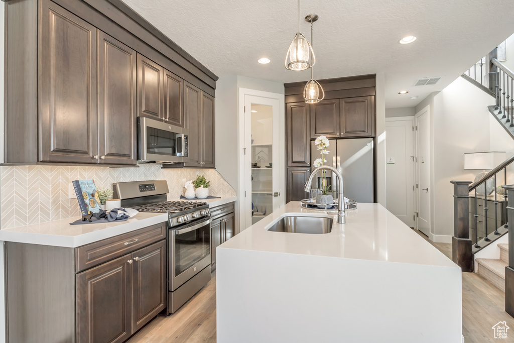 Kitchen with sink, light hardwood / wood-style flooring, hanging light fixtures, stainless steel appliances, and a center island with sink