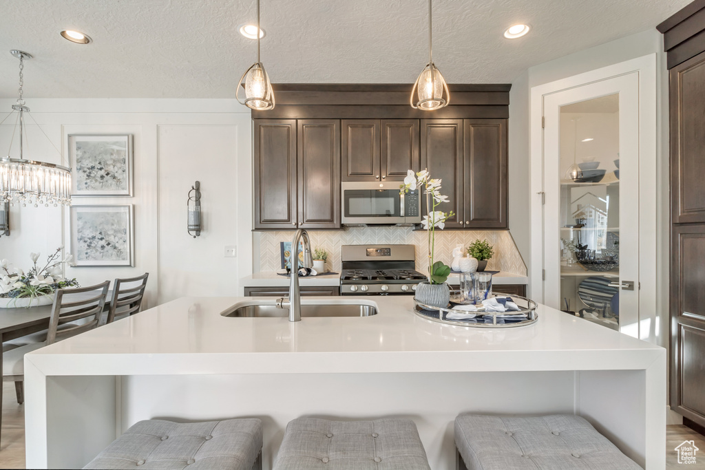 Kitchen featuring pendant lighting, stainless steel appliances, a kitchen island with sink, and a breakfast bar area