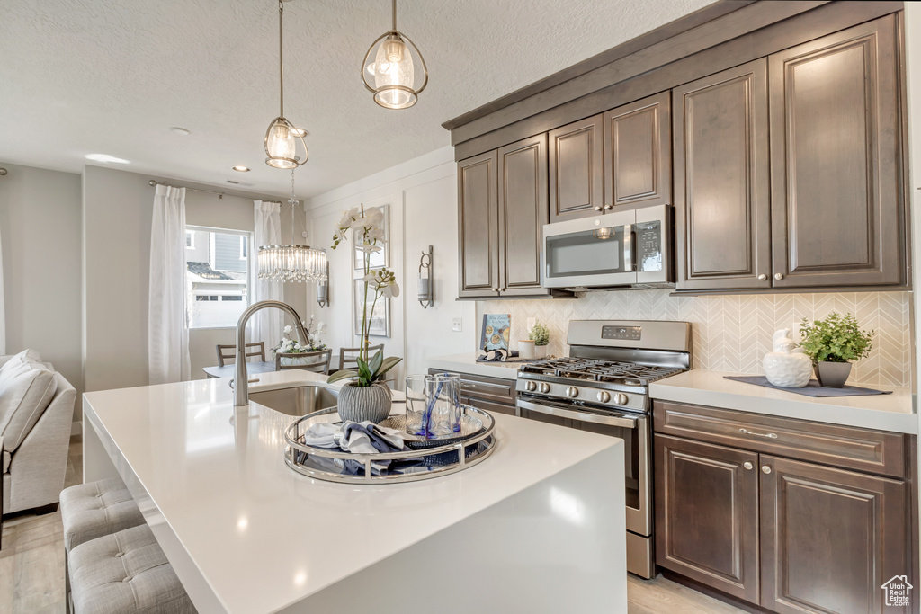 Kitchen with appliances with stainless steel finishes, decorative light fixtures, an island with sink, decorative backsplash, and dark brown cabinets