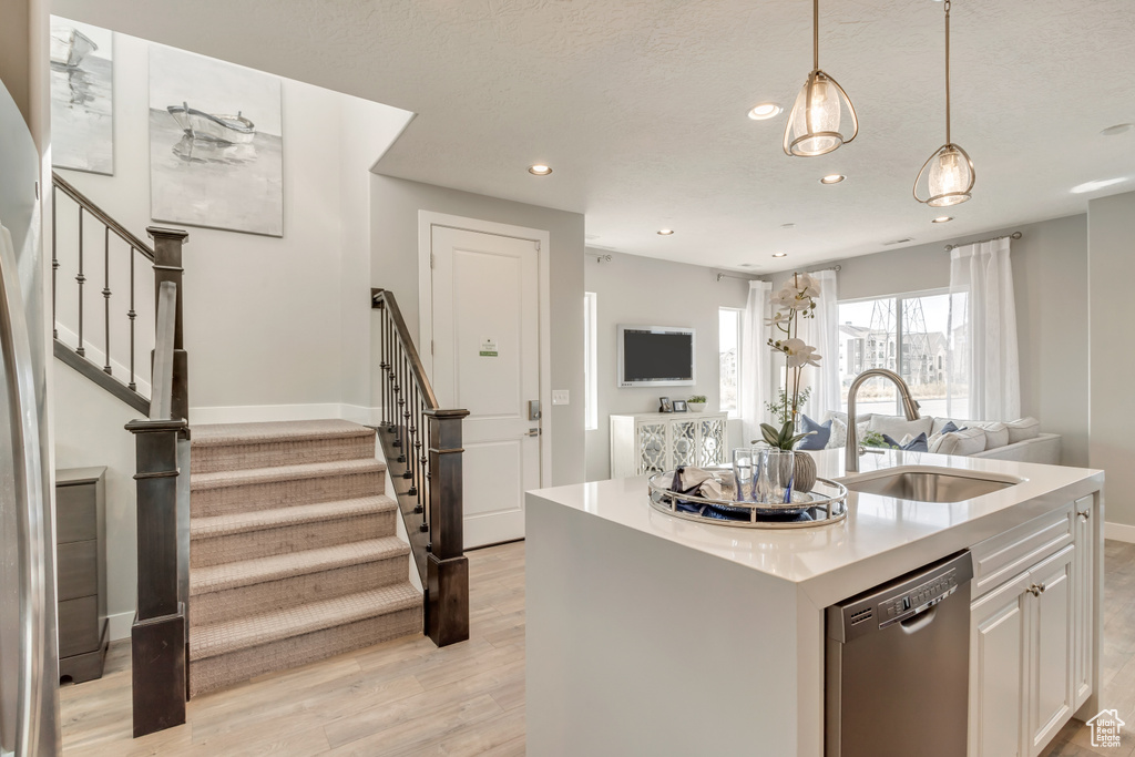 Kitchen with decorative light fixtures, sink, white cabinets, stainless steel dishwasher, and a center island with sink