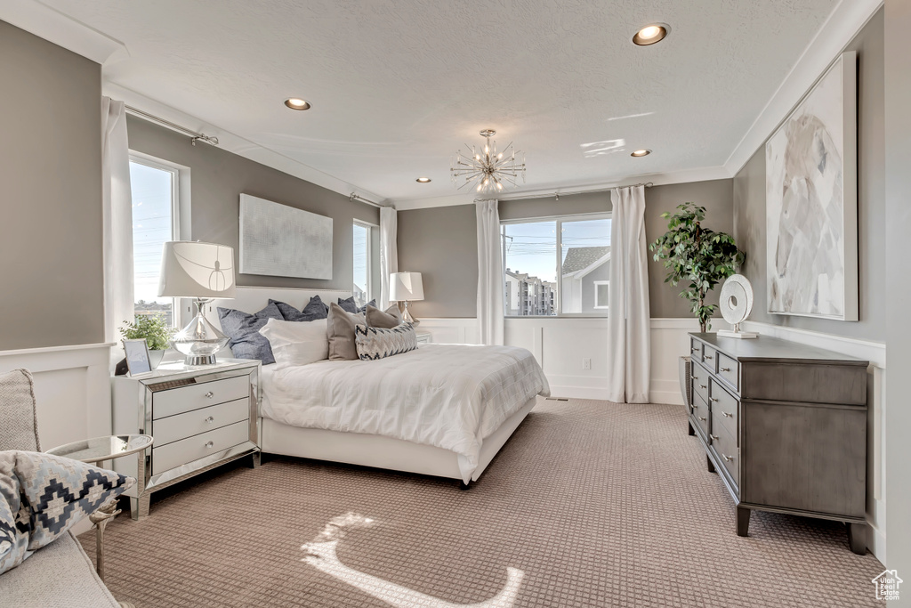 Carpeted bedroom with crown molding, a textured ceiling, and a notable chandelier