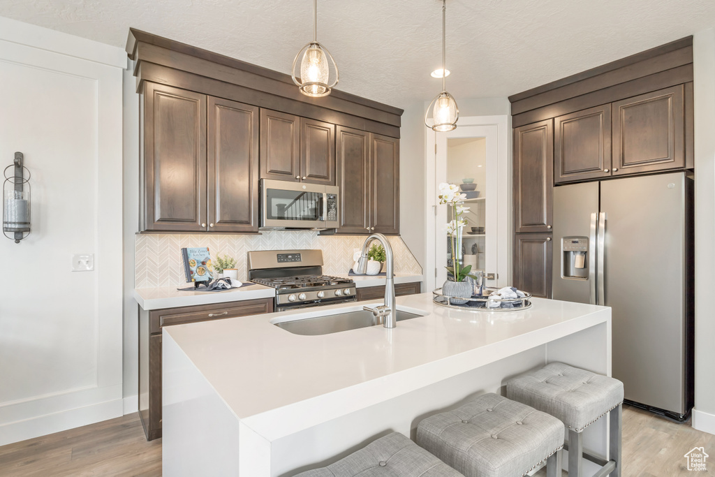 Kitchen with appliances with stainless steel finishes, a kitchen island with sink, sink, and decorative backsplash