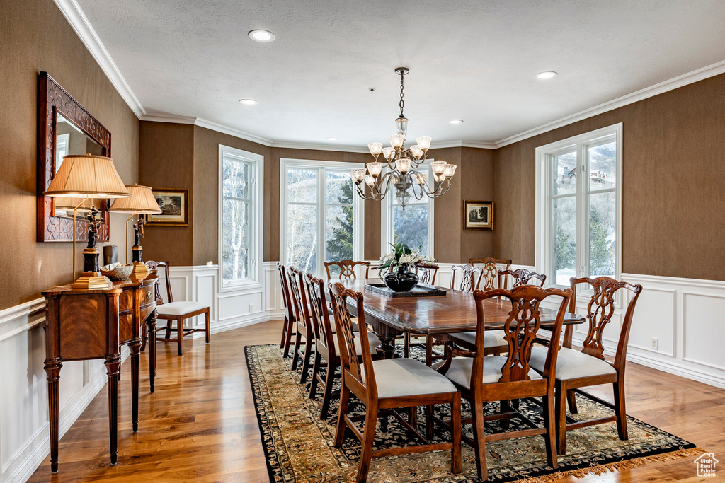 Dining area with light wood-type flooring, a decorative wall, a chandelier, recessed lighting, and ornamental molding