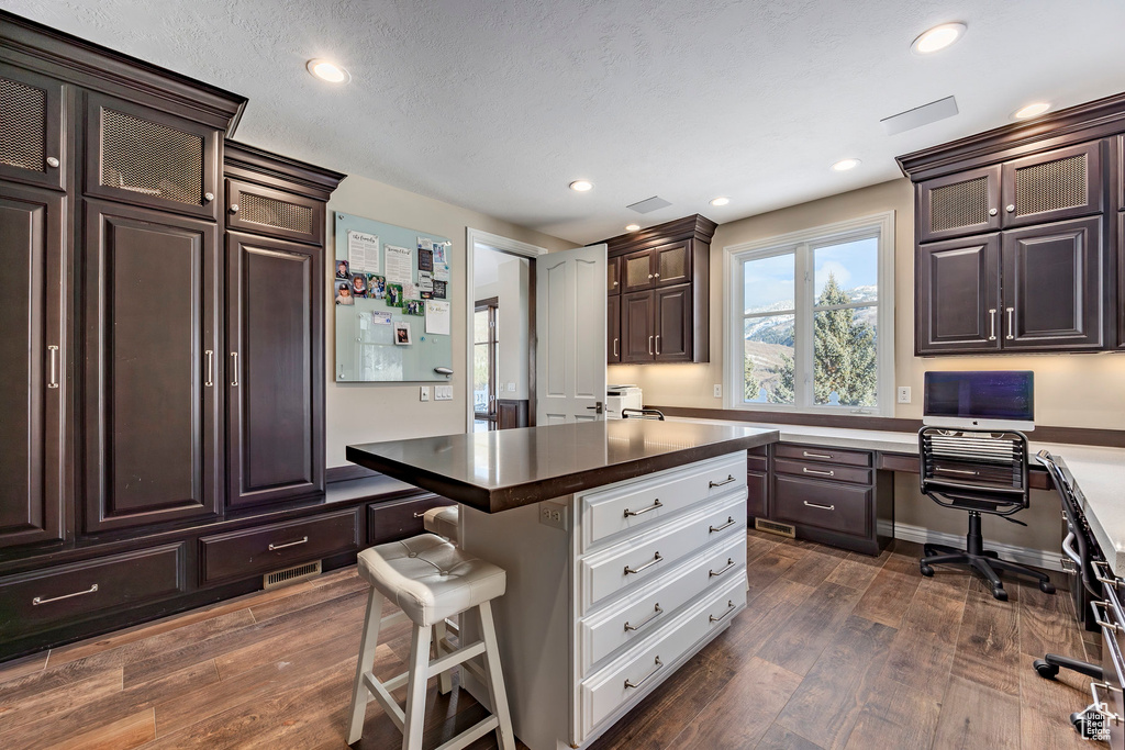 Kitchen featuring dark brown cabinets, a kitchen breakfast bar, dark wood-style floors, recessed lighting, and glass insert cabinets