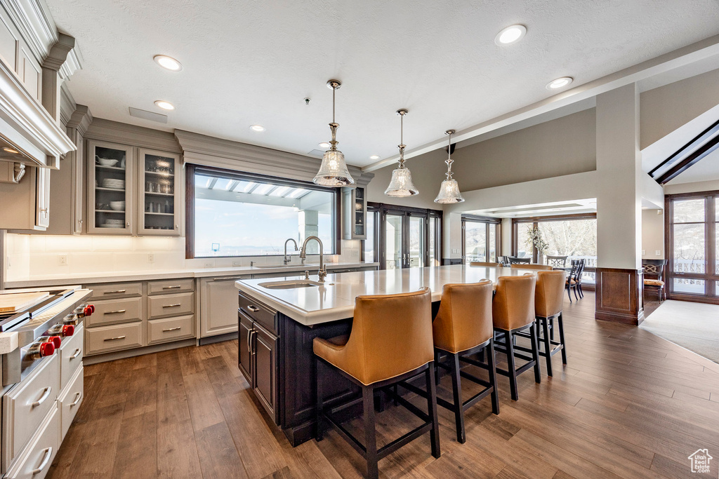 Kitchen with a sink, light countertops, a breakfast bar area, dark wood-type flooring, and a kitchen island with sink