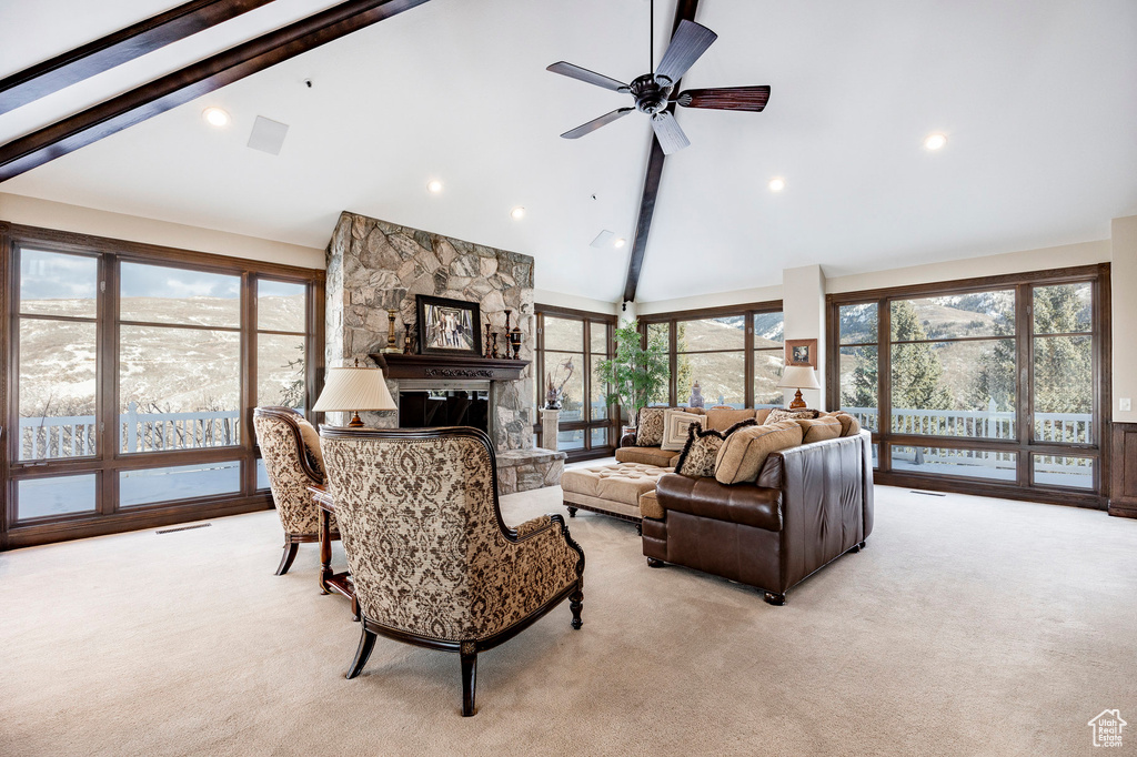 Living area with beamed ceiling, high vaulted ceiling, a stone fireplace, light colored carpet, and ceiling fan