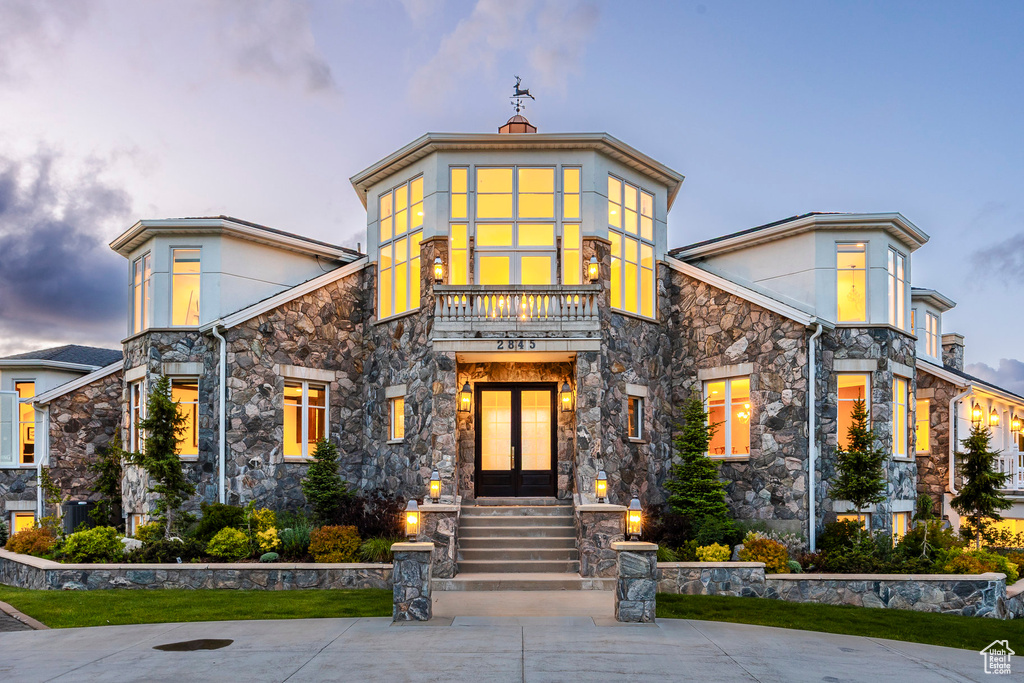 Modern home featuring stone siding, french doors, stucco siding, and a balcony