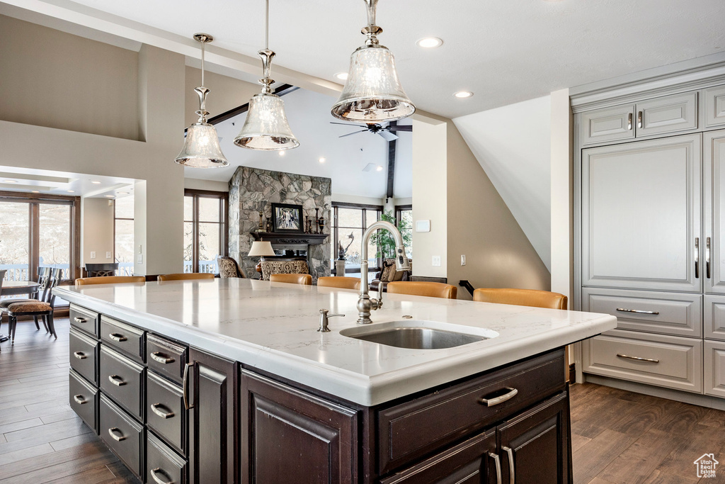 Kitchen with a sink, open floor plan, dark wood-style floors, light stone counters, and pendant lighting