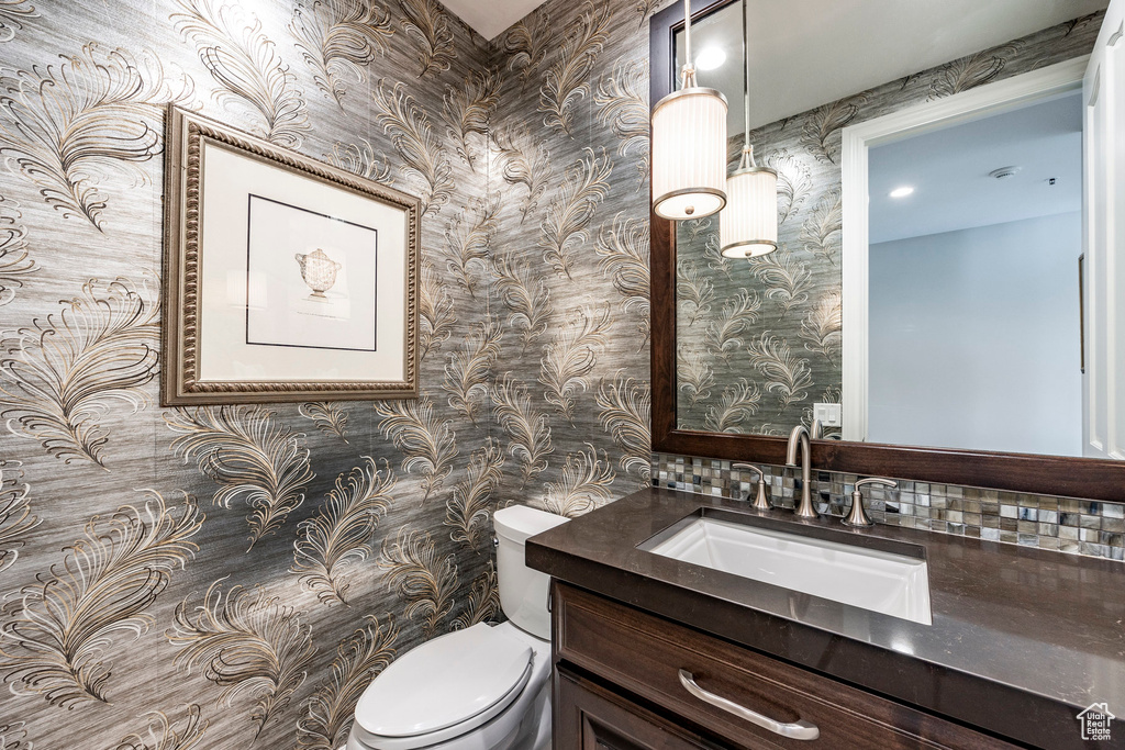 Bathroom featuring wallpapered walls, toilet, and vanity