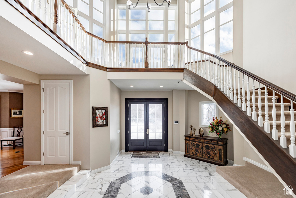 Entrance foyer with a towering ceiling, a chandelier, stairway, french doors, and baseboards