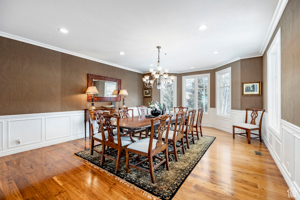 Dining space featuring a decorative wall, a chandelier, light wood-style floors, recessed lighting, and wainscoting