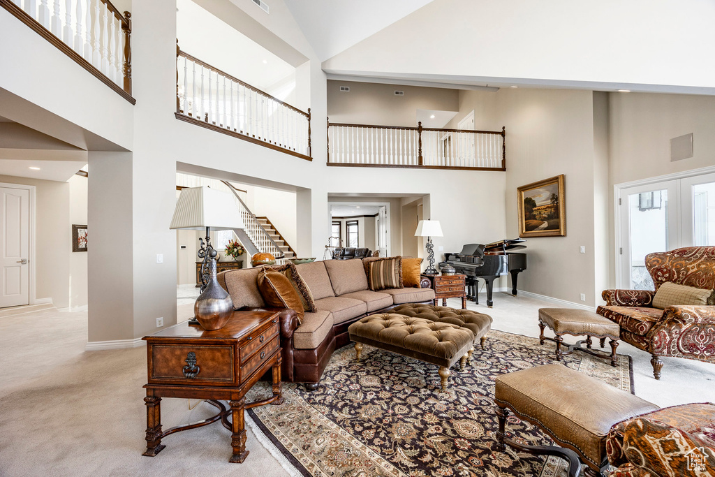 Living area featuring light carpet, a towering ceiling, stairs, and baseboards