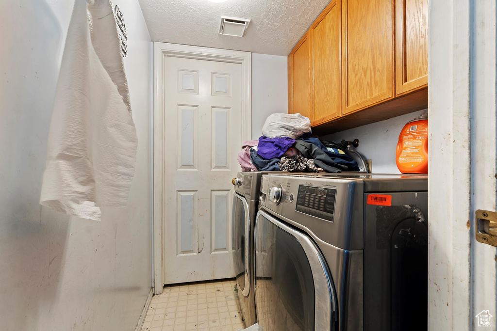 Laundry area featuring independent washer and dryer, cabinets, and a textured ceiling