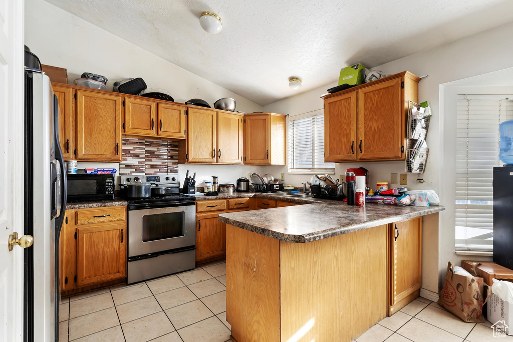 Kitchen featuring kitchen peninsula, lofted ceiling, stainless steel range with electric cooktop, light tile patterned floors, and fridge with ice dispenser