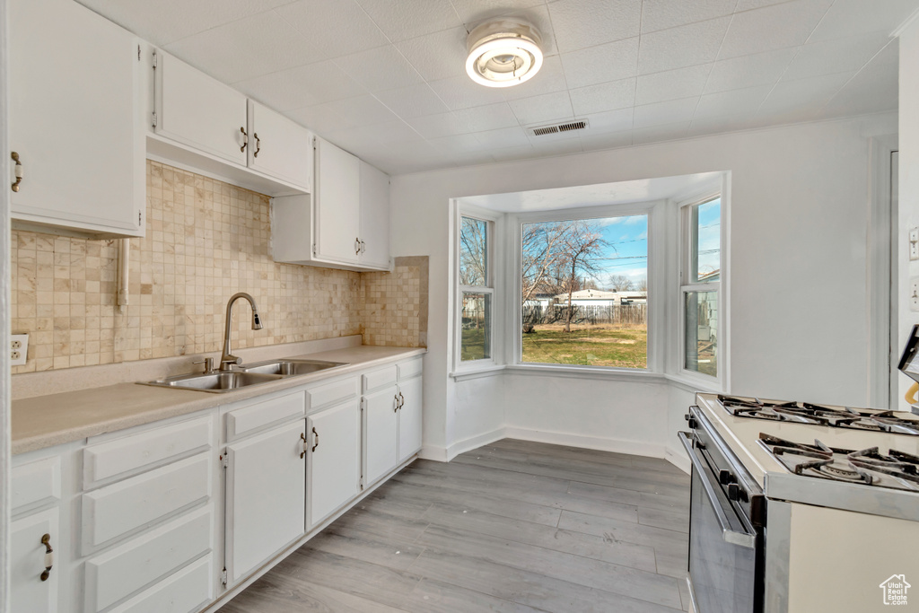 Kitchen with white cabinetry, white gas range, light hardwood / wood-style flooring, sink, and backsplash