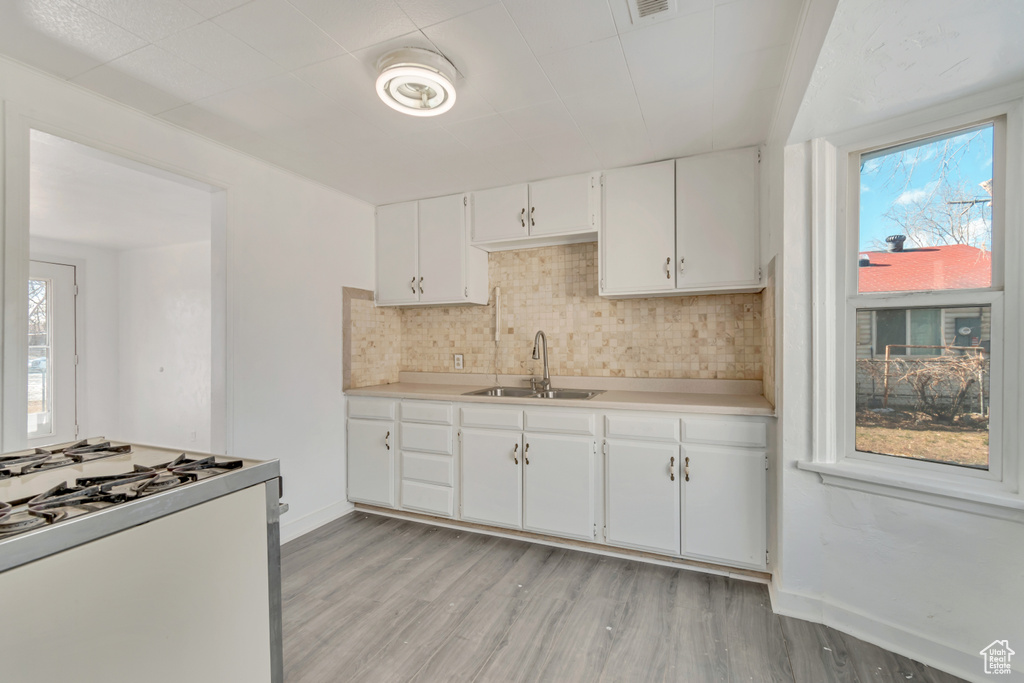 Kitchen featuring light hardwood / wood-style flooring, sink, white cabinetry, range with gas stovetop, and tasteful backsplash