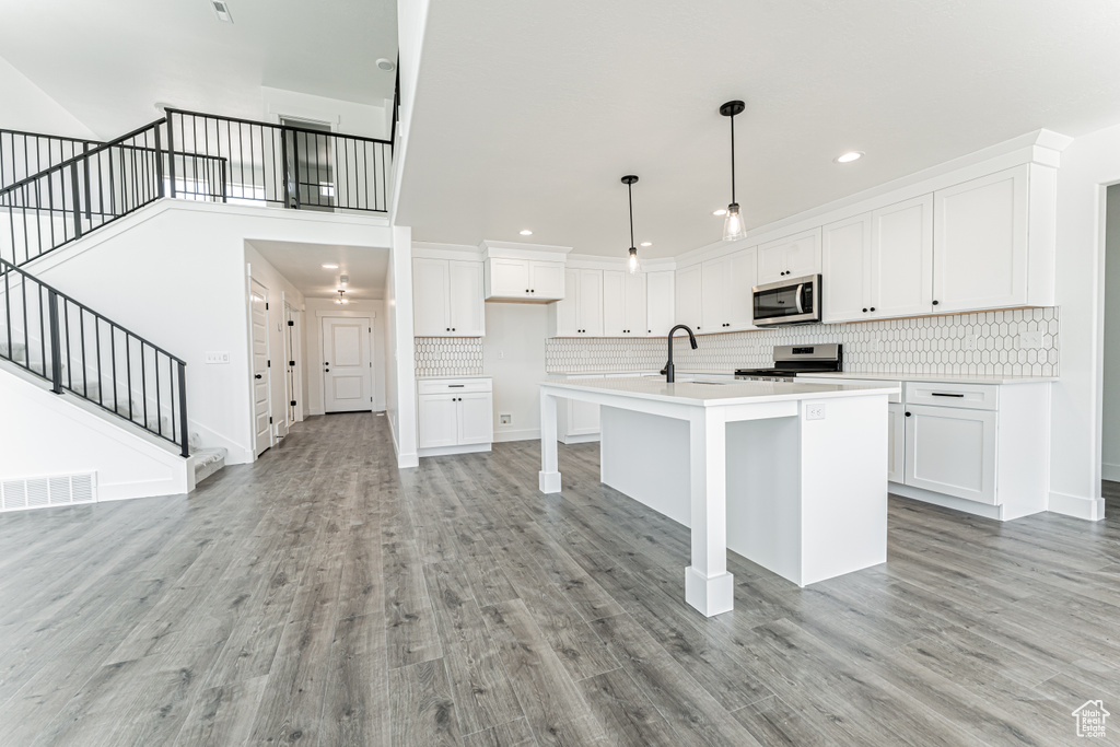 Kitchen featuring appliances with stainless steel finishes, white cabinets, light wood-type flooring, backsplash, and recessed lighting