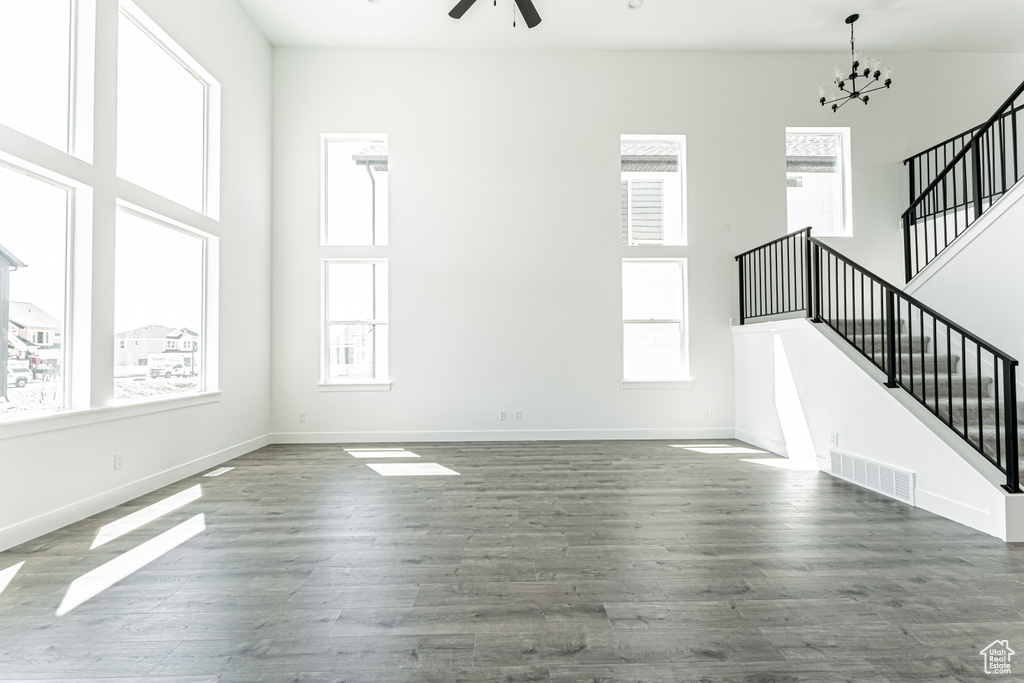 Unfurnished living room with healthy amount of natural light, stairway, ceiling fan, baseboards, and a towering ceiling
