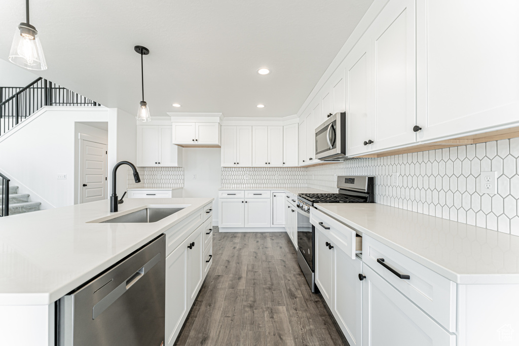 Kitchen with stainless steel appliances, a sink, backsplash, wood finished floors, and light countertops