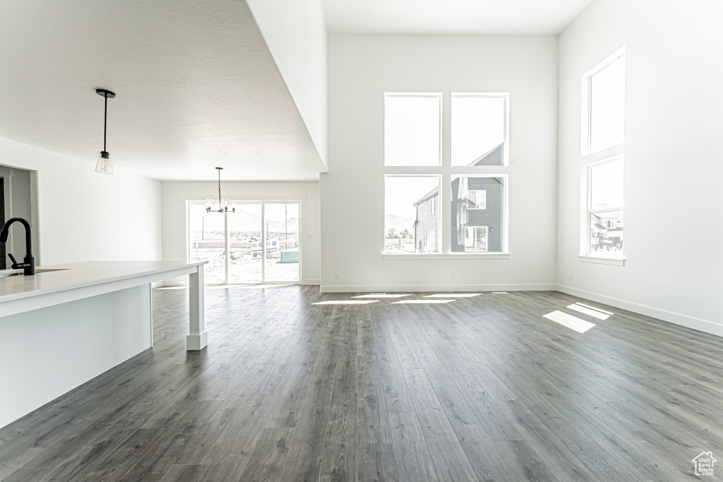 Unfurnished living room featuring dark wood finished floors, a chandelier, a sink, baseboards, and a high ceiling