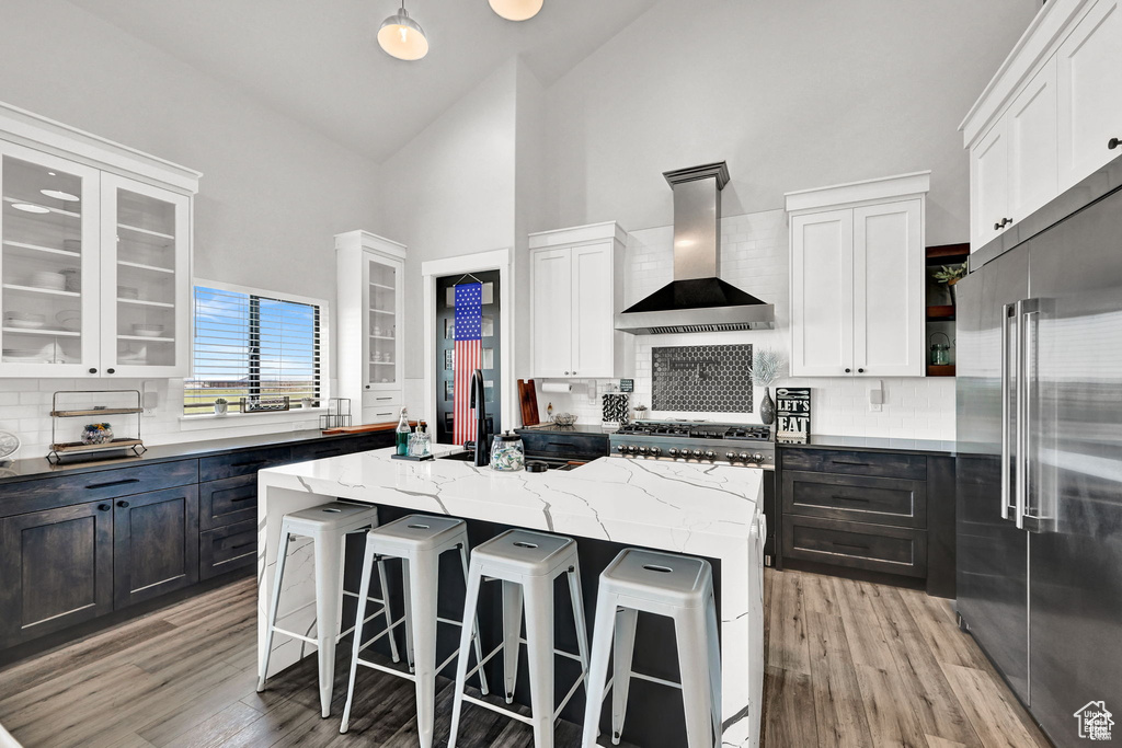 Kitchen with glass insert cabinets, high end fridge, a center island, and wall chimney range hood