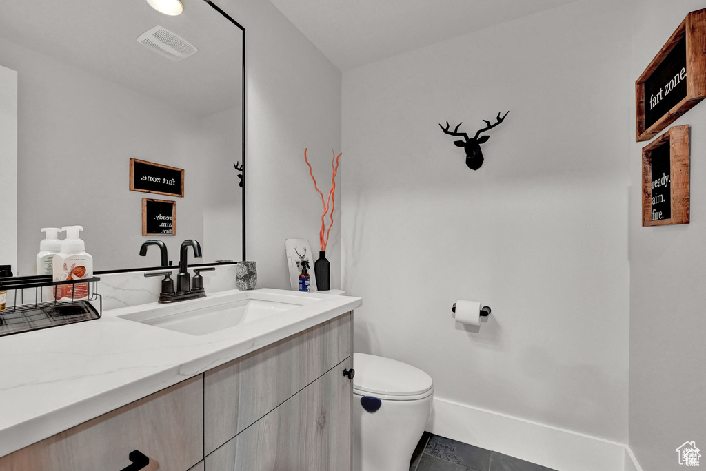 Half bath with visible vents, vanity, baseboards, and toilet