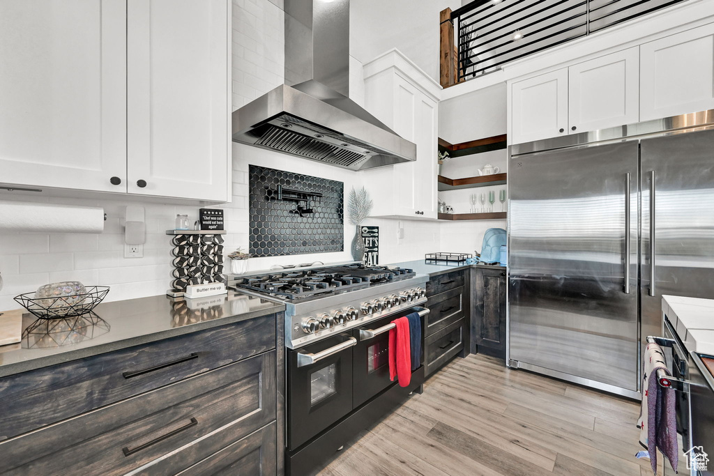 Kitchen featuring wall chimney range hood, white cabinetry, dark countertops, and high end appliances
