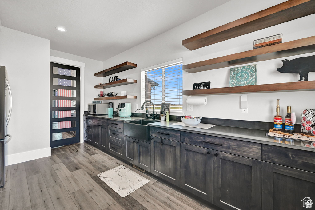 Kitchen featuring a sink, recessed lighting, light wood finished floors, dark cabinets, and open shelves