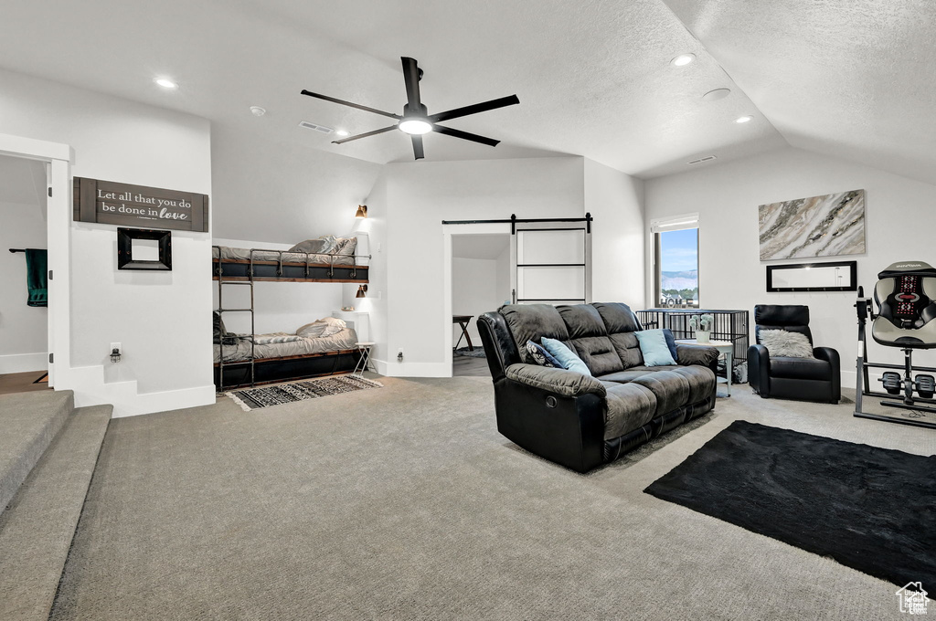 Living room with ceiling fan, vaulted ceiling, light colored carpet, a barn door, and a textured ceiling