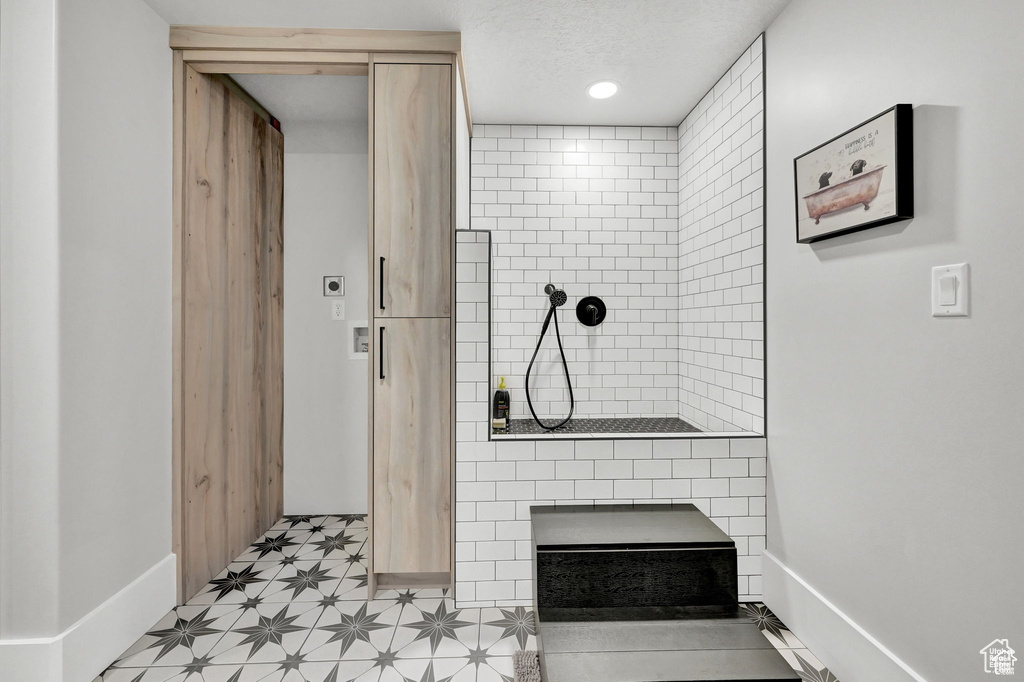Full bath featuring baseboards, a textured ceiling, tiled shower, and tile patterned floors