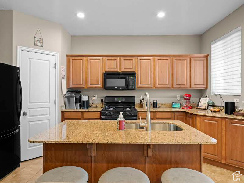 Kitchen with an island with sink, black appliances, light stone countertops, and a breakfast bar area