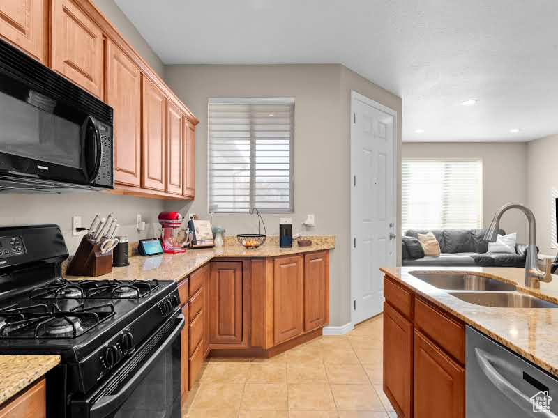 Kitchen with light tile patterned floors, sink, black appliances, and light stone counters