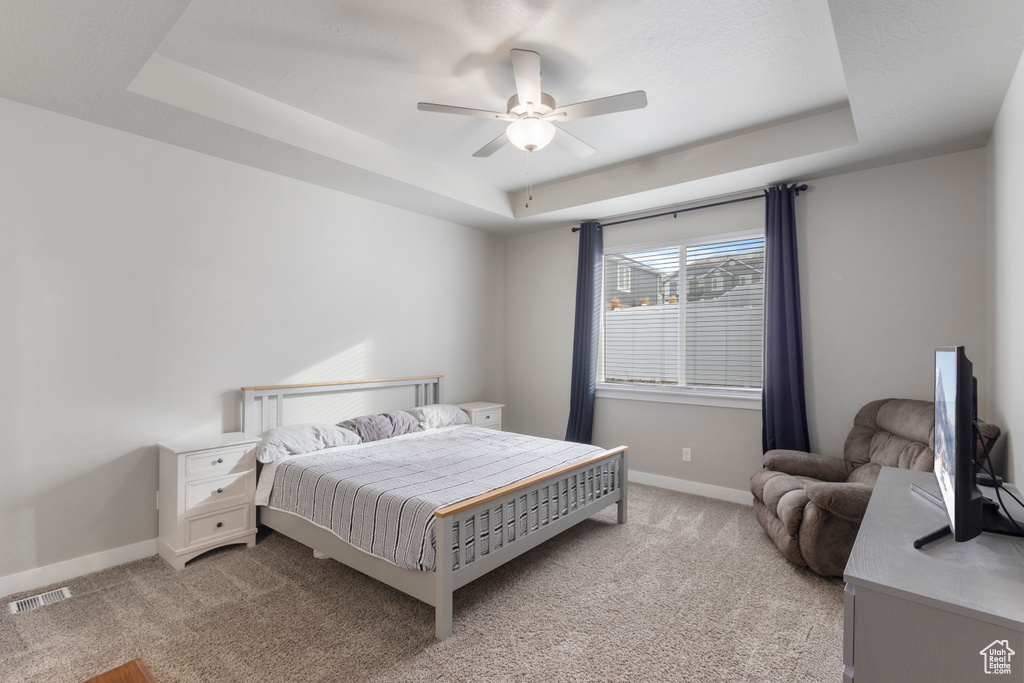 Bedroom with a tray ceiling, light carpet, and ceiling fan