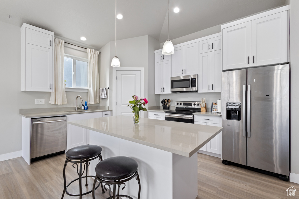Kitchen with white cabinetry, hanging light fixtures, a center island, sink, and appliances with stainless steel finishes