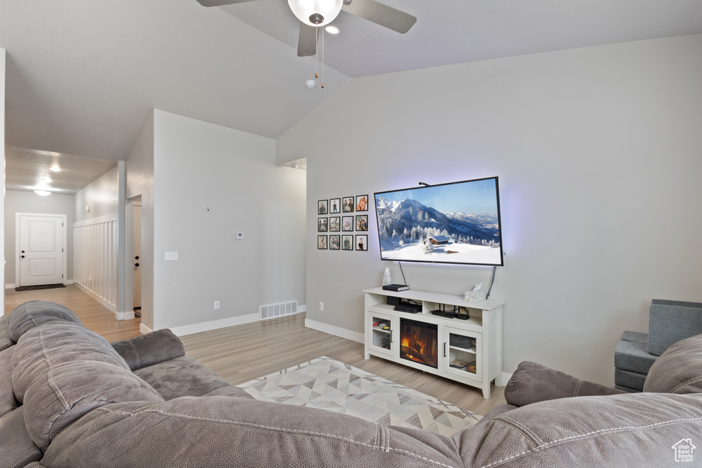 Living room featuring light wood-type flooring, ceiling fan, vaulted ceiling, and a fireplace