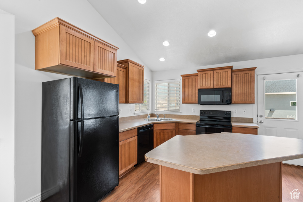 Kitchen featuring black appliances, vaulted ceiling, light wood finished floors, light countertops, and a kitchen island
