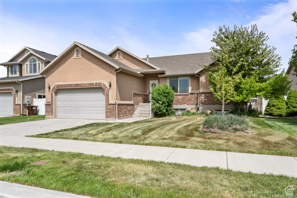 View of front of home with an attached garage, stucco siding, a front yard, brick siding, and driveway