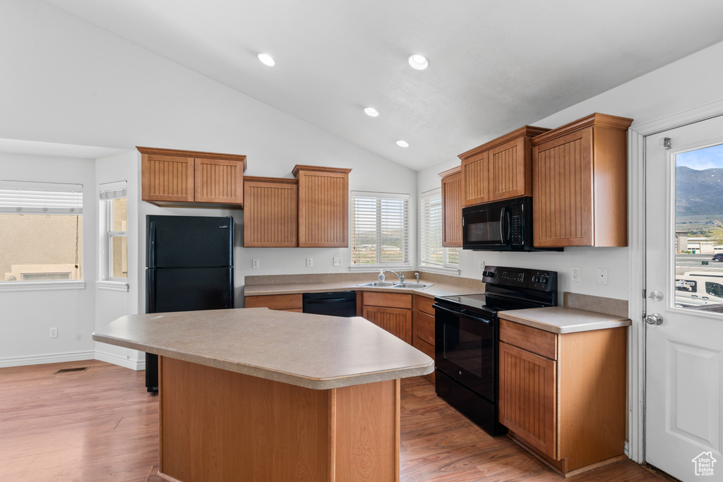 Kitchen with black appliances, light countertops, light wood-style flooring, and vaulted ceiling