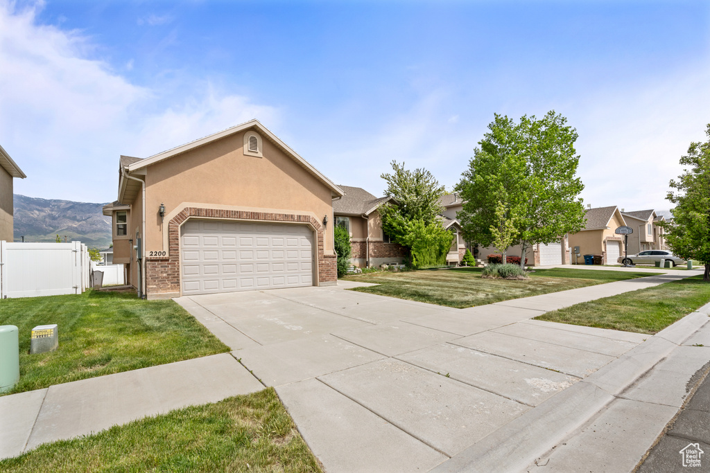 Ranch-style house featuring concrete driveway, a front lawn, an attached garage, and fence