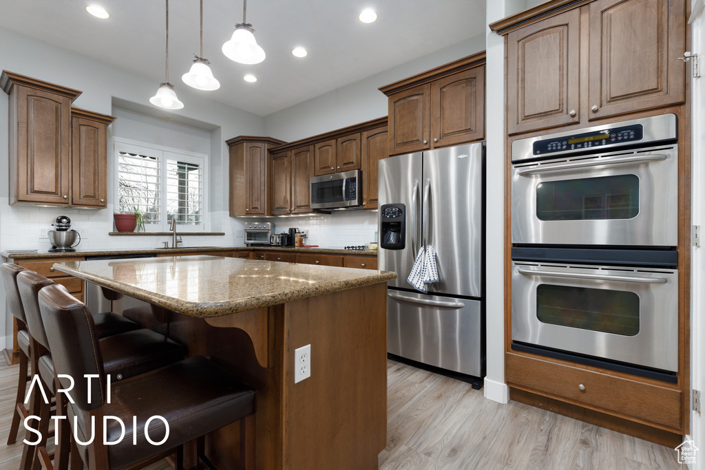 Kitchen with appliances with stainless steel finishes, a kitchen bar, light stone counters, a center island, and light hardwood / wood-style floors