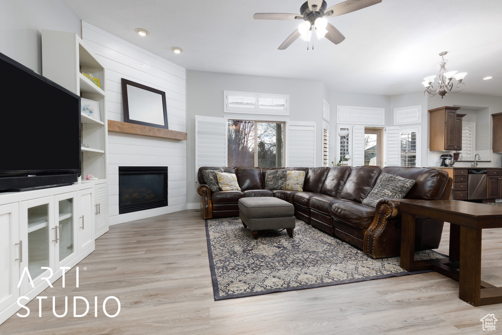 Living room with ceiling fan with notable chandelier, light hardwood / wood-style flooring, sink, and a fireplace