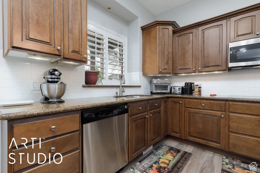 Kitchen featuring sink, stone counters, light wood-type flooring, stainless steel appliances, and decorative backsplash