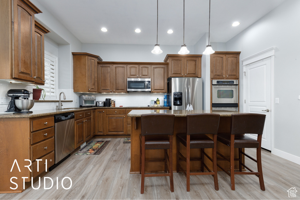 Kitchen with stainless steel appliances, dark stone counters, decorative light fixtures, backsplash, and a kitchen island