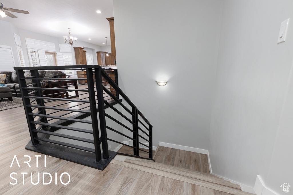 Stairway with hardwood / wood-style flooring and ceiling fan with notable chandelier