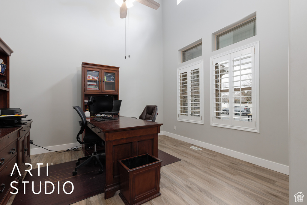 Home office with ceiling fan, light wood-type flooring, and a towering ceiling