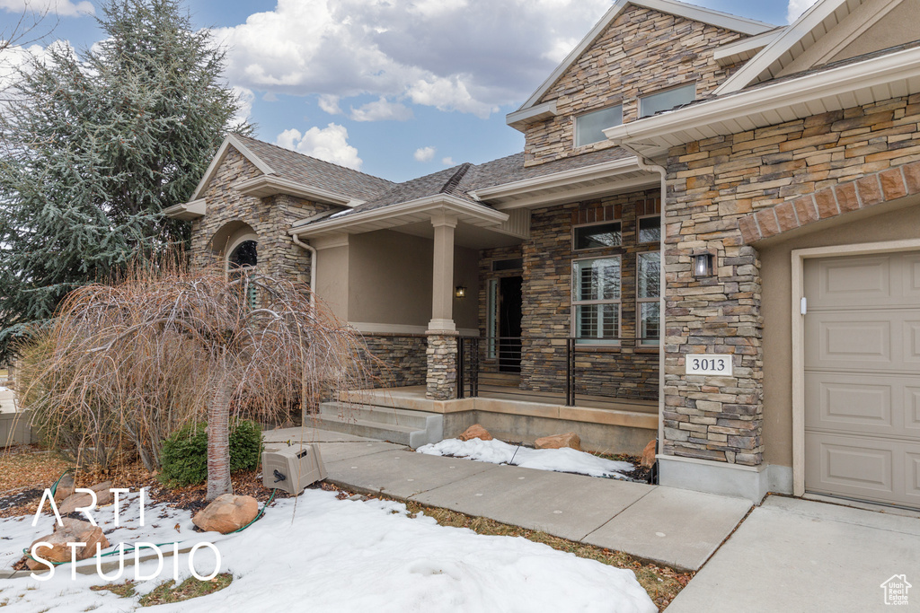 Snow covered property entrance featuring a porch and a garage